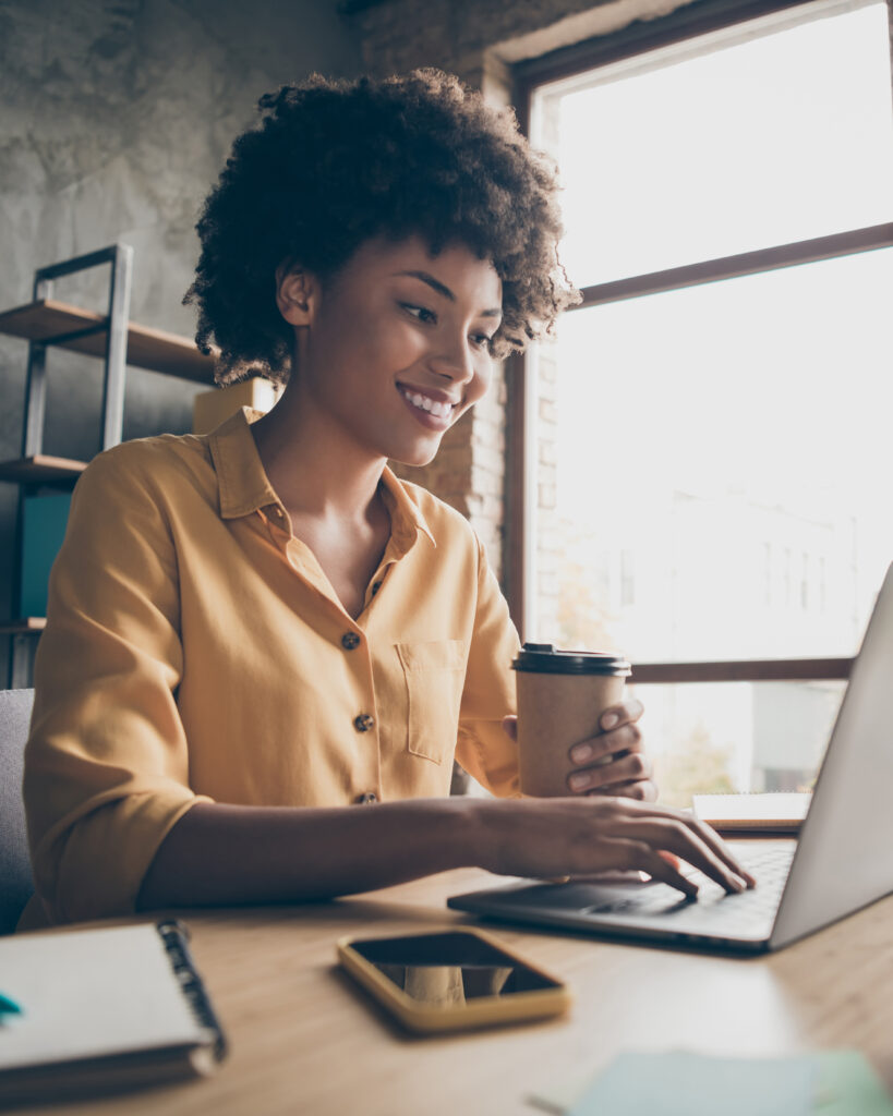 Profile side photo of charming smart afro american girl entrepreneur use computer, work training company career development seminar sit table hold takeout mug hot beverage in loft office