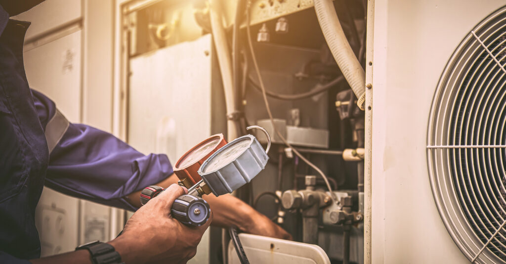 Heat and Air Conditioning, HVAC system service technician using measuring manifold gauge checking refrigerant and filling industrial air conditioner after duct cleaning maintenance outdoor compressor.