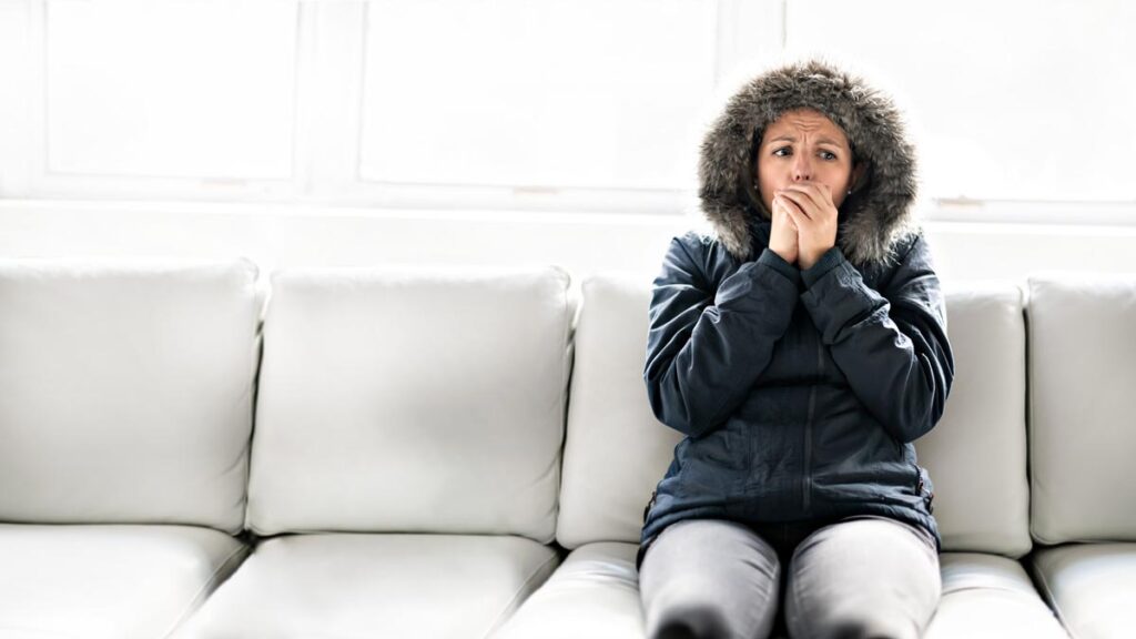 Cold woman sitting on sofa in winter jacket