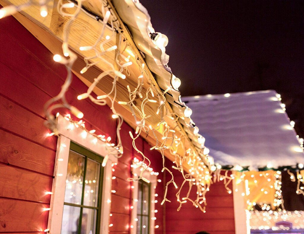 Red house with white Christmas lights along the roof and windows.