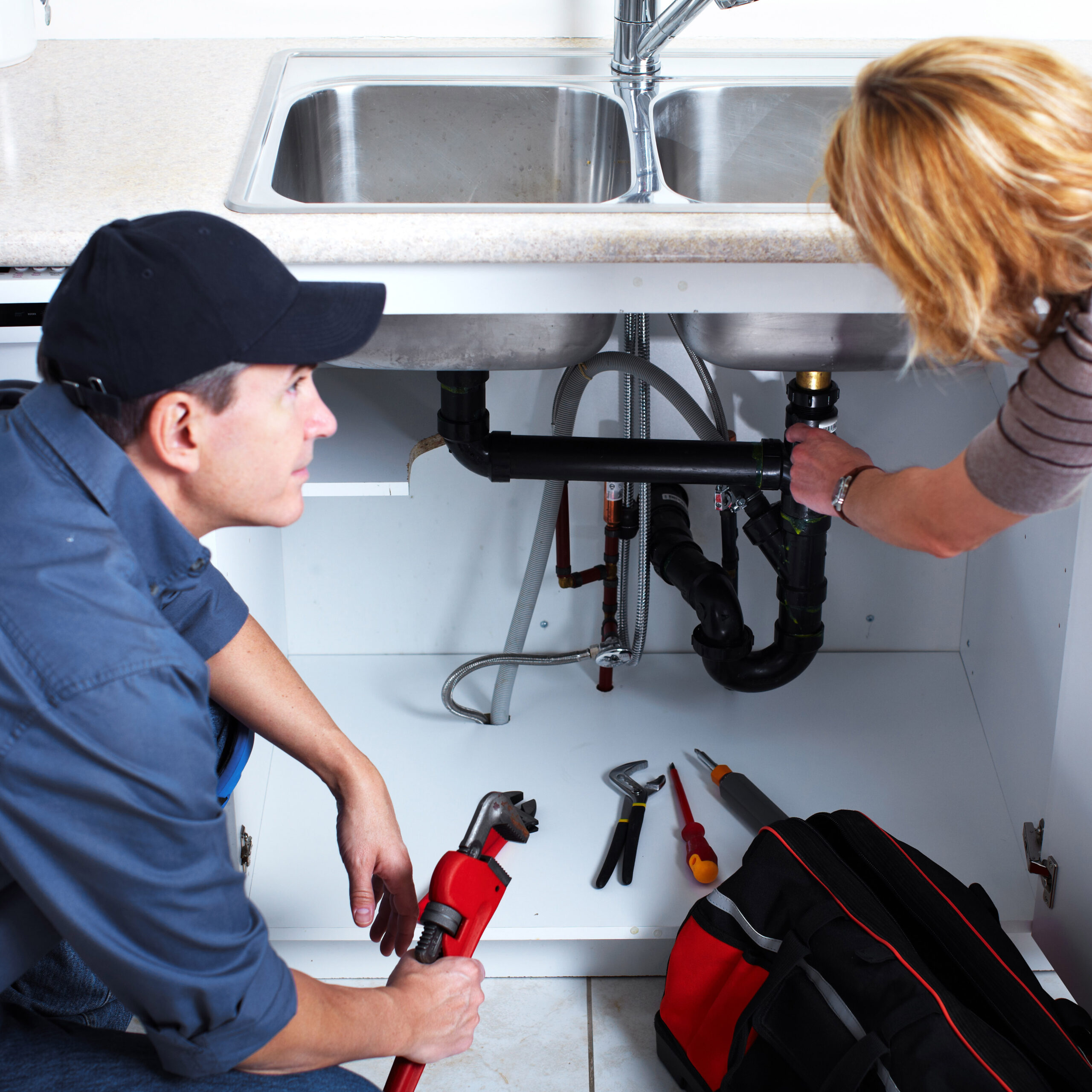 plumber and home owner looking at the pipes under the kitchen sink