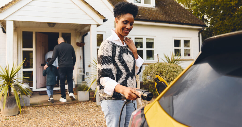 Woman plugging in electric charger into car With Family Outside House