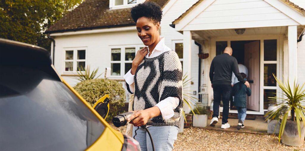Woman plugging in electric charger into car With Family Outside House