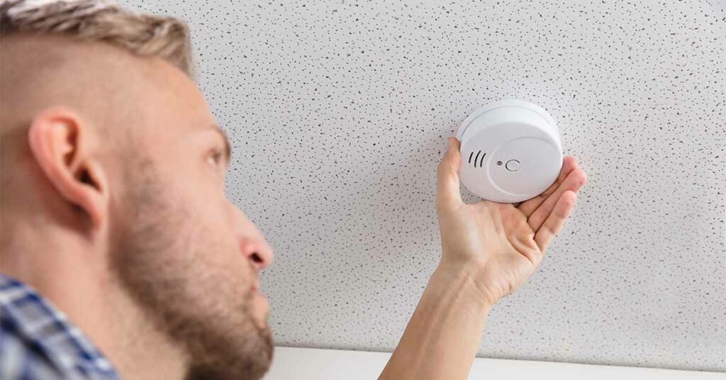 Low Angle View Of A Person's Hand Installing Smoke Detector On Ceiling Wall At Home