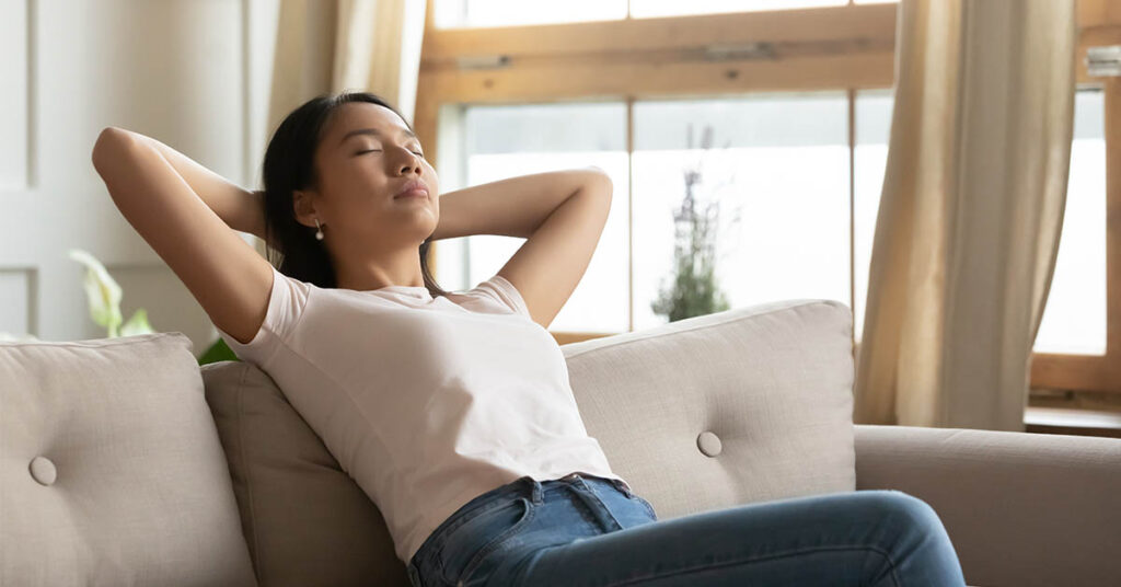 Calm Asian young woman sit relax on sofa in living room take nap or daydream, peaceful Vietnamese millennial girl rest on couch at home, breathe fresh air, relaxation, stress free concept