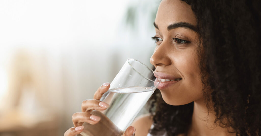 Healthy Liquid. Smiling Black Woman Drinking Water From Glass And Looking Away, Closeup Image With Selective Focus