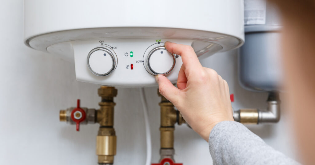 Female hand puts thermostat of electric water heater (boiler) in economy mode. Household energy saving equipment