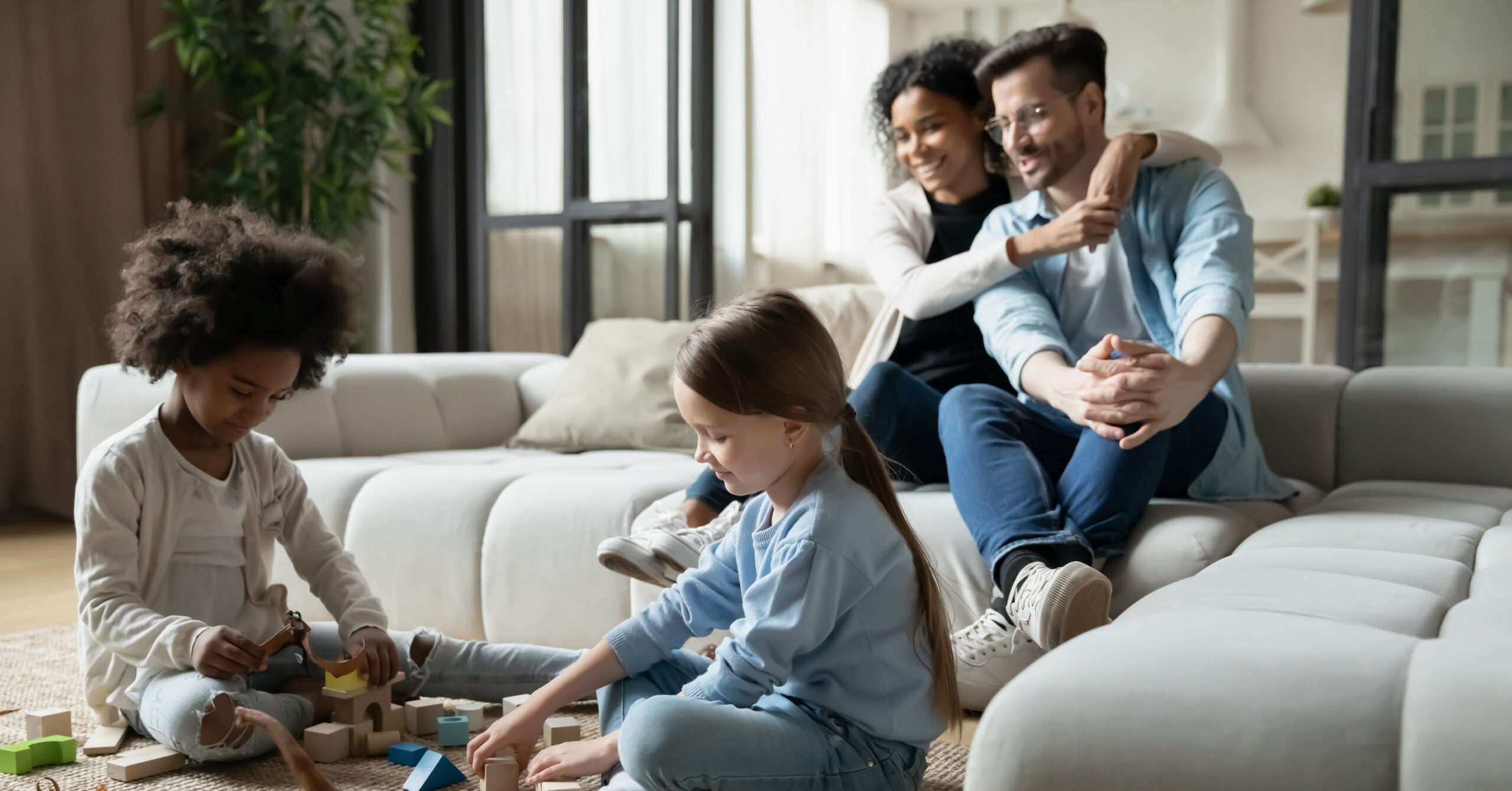 Couple sitting on a couch with 2 kids playing on the floor