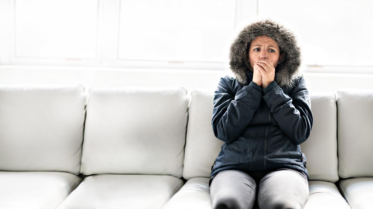 woman sitting on a couch in a winter coat while warming her hands