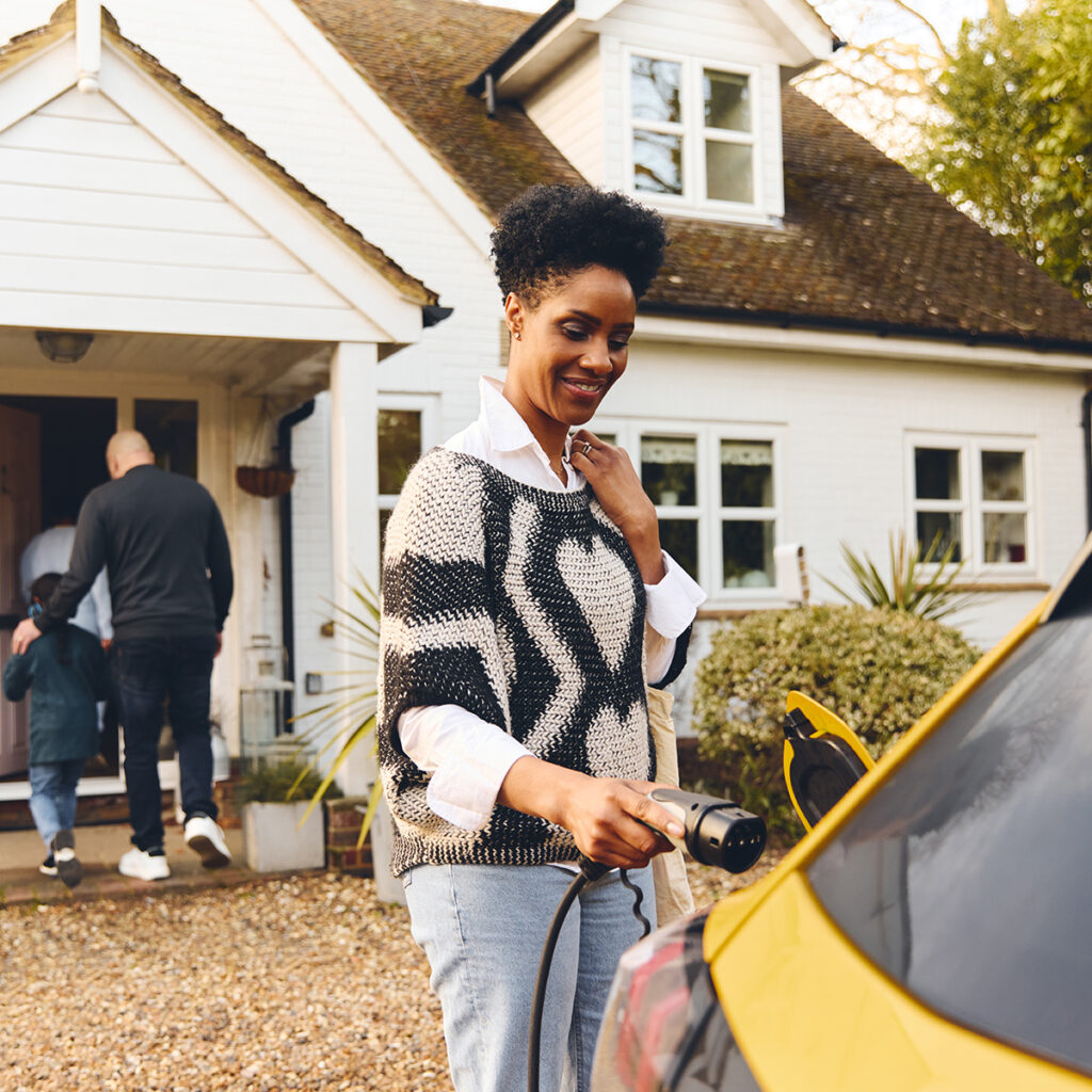 Woman plugging in electric charger into car With Family Outside House