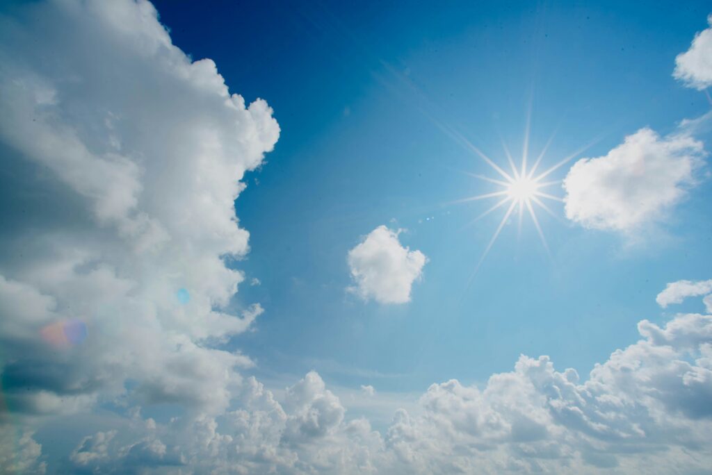 Sun shining in the blue sky surrounded by a few clouds